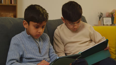 Two-Young-Boys-Sitting-On-Sofa-At-Home-Playing-Games-Or-Streaming-Onto-Digital-Tablets-8